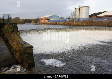 Weir am Fluss irwell mit Industriegebäuden und Silos im Hintergrund in Bury lancashire UK Stockfoto