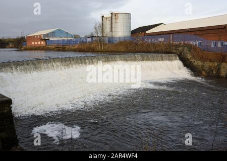 Weir am Fluss irwell mit Industriegebäuden und Silos im Hintergrund in Bury lancashire UK Stockfoto