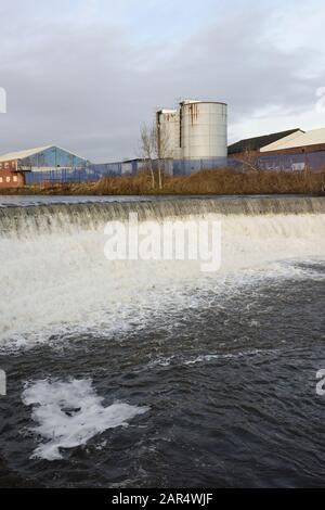 Weir am Fluss irwell mit Industriegebäuden und Silos im Hintergrund in Bury lancashire UK Stockfoto