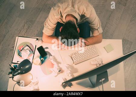 Draufsicht über den müden Mann, der auf dem Tisch im Büro schläft Stockfoto