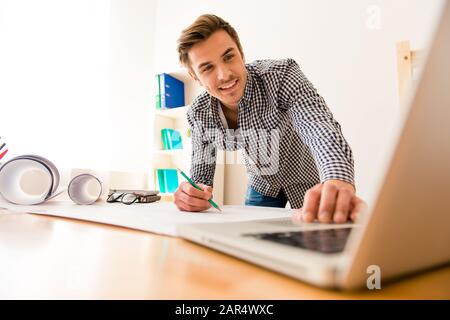 Fröhlicher junger Mann, der mit einem Laptop sein Schema kreieren kann Stockfoto