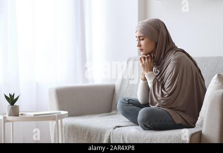 Depressive muslimische Frau im Hijab, die auf dem Sofa zu Hause aufgeregt sitzt Stockfoto