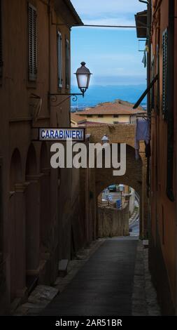 Eine enge Straße/Passage zwischen zwei roten Ziegelmauern in einer alten mittelalterlichen italienischen Stadt mit schöner Aussicht und Carabinieri (Polizei) Schild an einer Wand Stockfoto