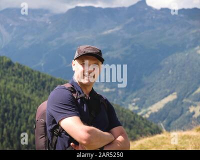 Porträt eines Mannes mit gekreuzten Armen, der im Sommer in den Alpen bei Saint-Luc weht und Rucksack wandert. Anniviers, Wallis, Schweiz Stockfoto