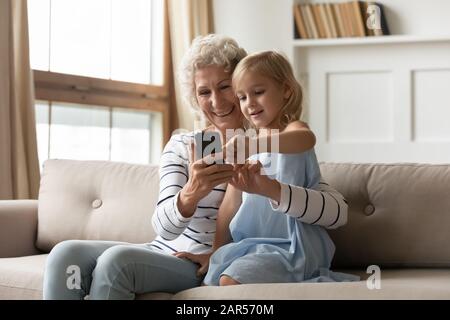 Frau mittleren Alters, die Smartphone mit einem liebenswerten Kindermädchen verwendet. Stockfoto