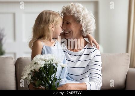 Fröhliche liebevolle Oma mittleren Alters, die Nasen mit Enkelin berührt. Stockfoto