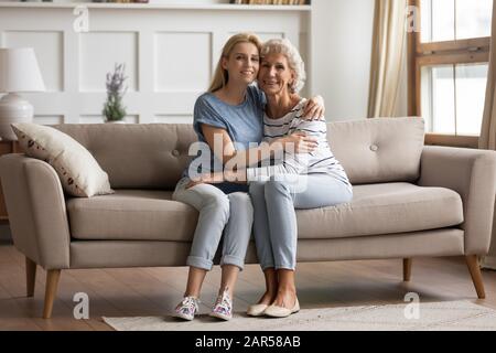 Porträt der lächelnden jungen blonden Frau, die ältere alte Mutter kuschelt. Stockfoto