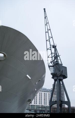 Ein Schiffsbogen und ein alter industrieller Dockseitenkran an den Royal Victoria Docks, London, Großbritannien Stockfoto