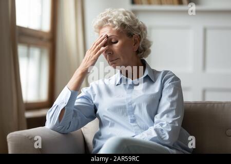 Frustrierte nervöse Frau im mittleren Alter, die die Stirn berührt. Stockfoto