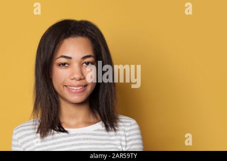 Lächelnde Mixed-Race-junge Frau im gestreiften Hemd auf gelbem Studiohintergrund Stockfoto