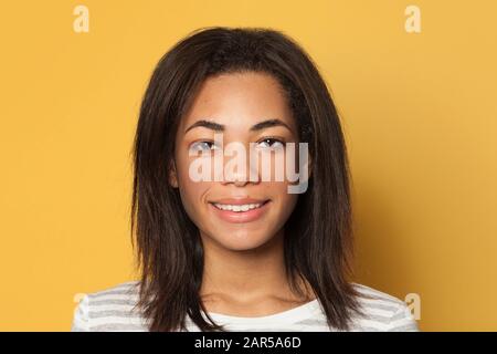 Fröhliche schöne brünette junge dunkelhäutige Frau auf gelbem Hintergrund, Studio-Porträt Stockfoto