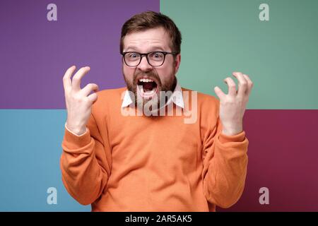Wütender bärtiger Mann schreit heftig, quetscht wütend die Hände und schaut auf die Kamera. Stockfoto