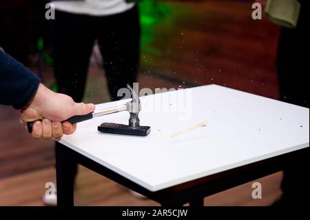 Der Hammer schlägt auf dem Tisch auf das alte Tastentelefon und die Bruchstücke fliegen auseinander Stockfoto