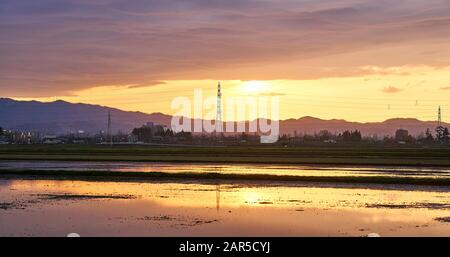 Strahlend orangefarbener Sonnenuntergang in Niigata, Japan, im frühen Frühjahr, bevor der Reis gepflanzt wurde. Stockfoto