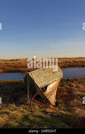 Ein beschädigtes altes Fischerboot aus Holz mit seinem Rostenden Metallanker, der auf den Gras-Ufern einer kleinen Küstenmeerwassermünde am St. Cyrus Beach liegt. Stockfoto