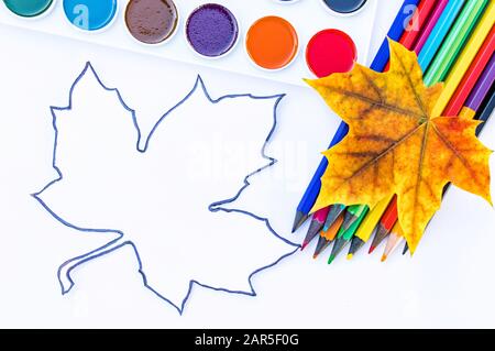 Bunte Herbstblätter, mehrfarbige Bleistifte und Lack zum Malen in der Nähe von Weißpapier mit Textstelle. Hintergrund mit Herbstlaub. Kopierbereich f Stockfoto