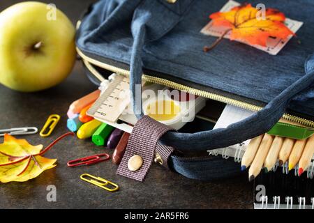 Zurück zum Schulkonzept. Schulzubehör mit blauem Rucksack auf dem Tisch. Stockfoto