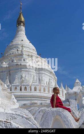 Junger buddhistischer Mönch, der im Februar auf der Myathindan Pagode (auch Hsinbyume Pagode genannt), Mingun, Myanmar (Birma), Asien sitzt Stockfoto