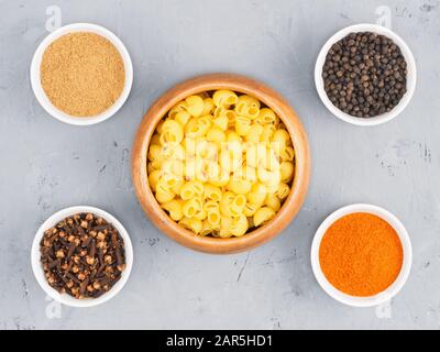 Pasta, schwarzer Pfeffer, rote Chili, Masala, Nelken in der Schüssel auf grauem Betongrund. Gesundes Esskonzept Stockfoto