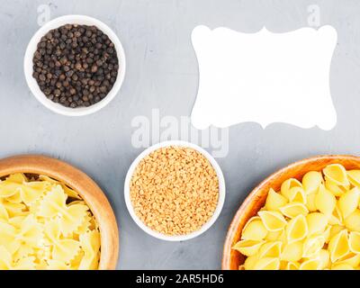 Verschiedene Nudelarten in Holzschüsseln, Fenugreek, schwarzer Pfeffer auf grauem Betonhintergrund mit Kopierraum. Gesundes Esskonzept Stockfoto