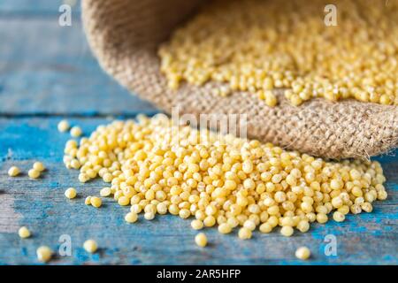 Rohe gelbe Hirse wird auf den blauen Bretter in der Nähe des Beutels verstreut. Nahaufnahme. Stockfoto