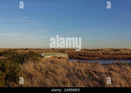 Ein verlassenes Altes Fischerboot aus Holz an den Ufern einer kleinen Estuary unter einem klaren blauen Himmel und goldenem Licht eines Winterabends. Stockfoto
