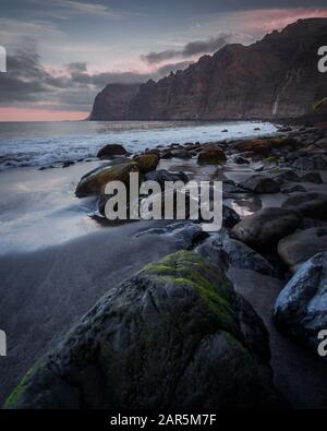 Vertikale Hochwinkelaufnahme der Steine am Strand Unter dem wolkenlosen Himmel bei Sonnenuntergang Stockfoto