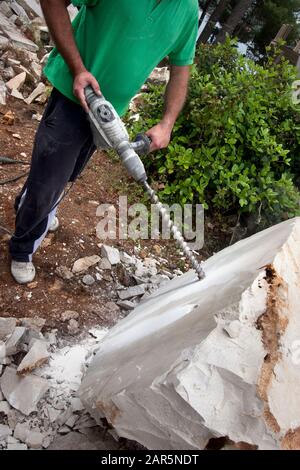 Man bohrt Löcher mit Bohrmaschine in Steinblock Stockfoto