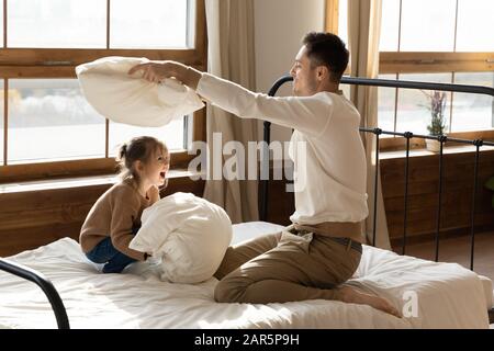 Glücklicher Vater, der mit der kleinen Tochter in den Kampf gegen Kopfkissen verwickelt war Stockfoto