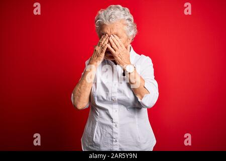 Ältere, schöne Frau, die ein elegantes Hemd trägt, das über isolierten roten Hintergründen steht und die Augen reibt, um Ermüdung und Kopfschmerzen, schläfrigen und müden Ausdruck zu erhalten. Stockfoto