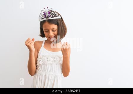 Wunderschönes Kindermädchen, das die Fürstenkrone trägt und über einem isolierten weißen Hintergrund steht, sehr glücklich und aufgeregt, indem sie Gewinnergeste mit erhobenen Armen tat, schmilzt Stockfoto