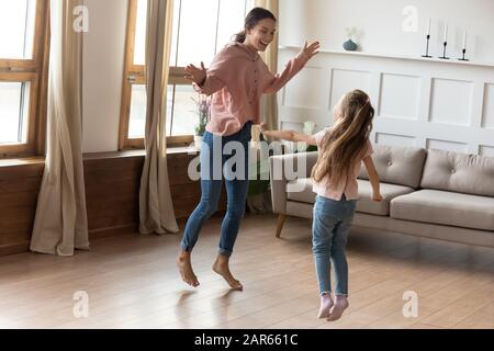 Überglücklich tanzten junge Mutter und kleine Tochter im Wohnzimmer Stockfoto