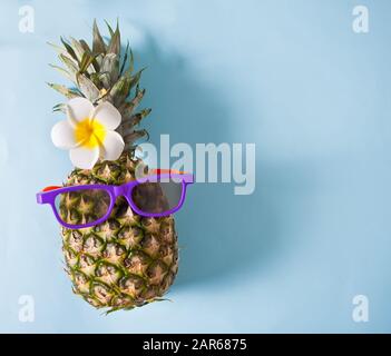 Saftige Ananas in Sonnenbrille auf blauem Hintergrund. Kopierbereich. Draufsicht. Stockfoto