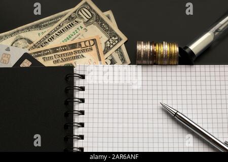 Leere Seite mit Stift, Dollar, Münzen, Kreditkarten, Sandglas auf schwarzem Hintergrund. Planung, Budgetierungs-Konzept Stockfoto