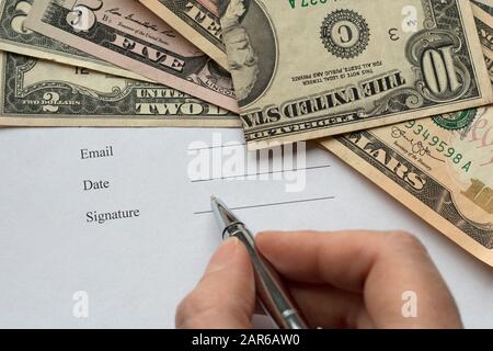Eine Person mit Ballpoint, die ein Dokument, eine Vereinbarung, einen Vertrag unterschreibt. Hintergrund des Dollars. Nahansicht. Stockbild Stockfoto