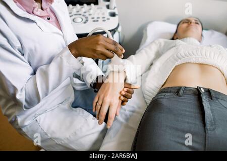 Nahaufnahme des afrikanischen Frauenarztes Hand mit Ultraschallscanner, der die Untersuchung an der Hand des jungen Patienten der Frau abhält Stockfoto