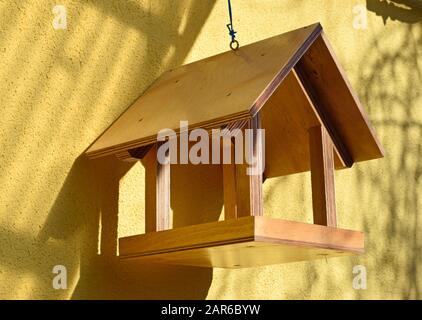 Vogelhaus aus Holz auf einem Hintergrund einer gelben Hauswand. Pflege der Vögel in der kalten Jahreszeit. Vogelzubringer in Form eines Hauses. Stockfoto