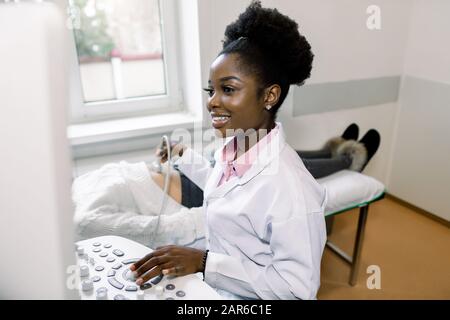 Professionelle afrikanische Ärztesiebung von Schwangeren per Ultraschall, Blick auf den Bildschirm und Lächeln Stockfoto