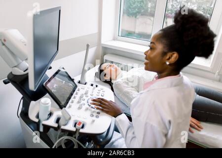Nahaufnahme des Sonografen des Arztes der Afrikanerin, der den Bauch einer jungen schwangeren Frau mit einem Ultraschallaufnehmer abtastet, der eine obstetrische Ultrasonographie macht Stockfoto