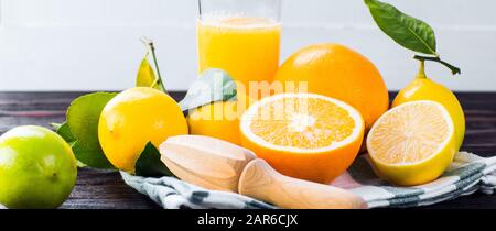 Frische Zitronen und Orangen mit grünen Blättern auf Holzgrund, Zitrussaft und Entsafter, langes Banner Stockfoto