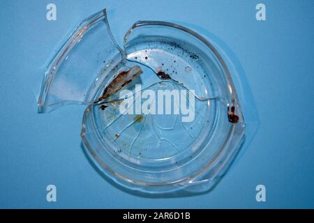 Backform aus zerbrochenem Glas, Draufsicht. Eine Glasform aus hitzebeständigem Glas, die im Backofen gerissen ist. Glasstücke aus einer Schüssel auf blauem Grund. Stockfoto