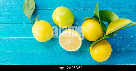 Frische Zitronen mit grünen Blättern auf blauem Holzhintergrund, langes Banner Stockfoto