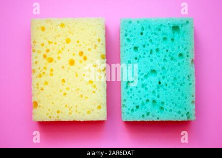 Grüner und gelber Schaumstoffschwamm zum Spülen von Geschirr. Weiche Waschtücher auf pinkfarbenem Hintergrund Draufsicht. Stockfoto