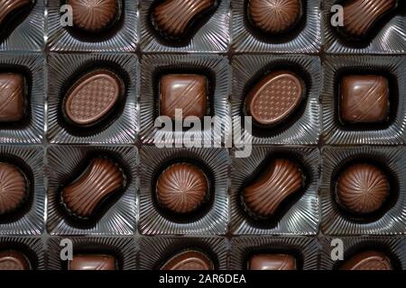 Verschiedene Pralinen in einer Schachtel mit Draufsicht. Süßigkeiten unterschiedlicher Form aus schwarzer Schokolade mit Füllungshintergrund. Schokoladendessspeisen. Stockfoto
