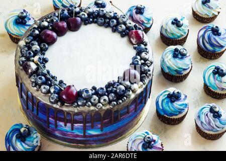 Heller festlicher blauer Kuchen mit Beeren und Schokolade und Cupcakes mit Sahne, Süßigkeiten-Bar, Sweet Bar Stockfoto