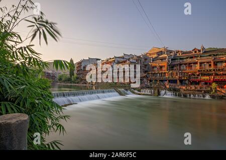 Feng Huang, China - August 2019: Lange Zeit Exposition des kleinen künstlichen Kaskadenwasserfalls am Fluss Tuo Jiang in der Altstadt von Fenghuang Kn Stockfoto