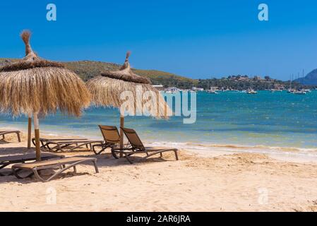 Strohschirme mit Sonnenliegen am Strand im schönen Port de Pollenca. Mallorca. Spanien Stockfoto