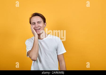 Ein Mann in weißem T-Shirt berührt sein Gesicht mit der Hand und lacht über die Kamera. Stockfoto