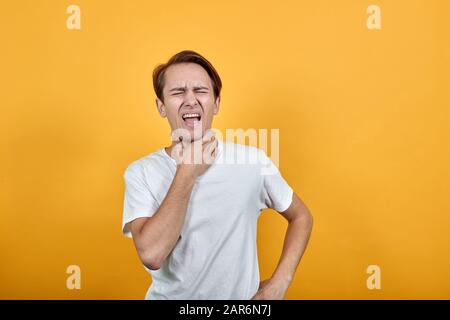 Mann mit Halsschmerzen, Halsschmerzen, die an seinem Hals auf gelbem Hintergrund festhalten Stockfoto