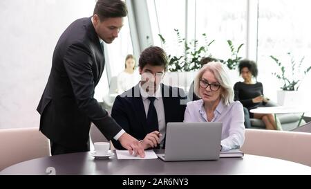 Selbstbewusster männlicher Vorgesetzter hilft Teamkollegen verschiedener Altersgruppen. Stockfoto